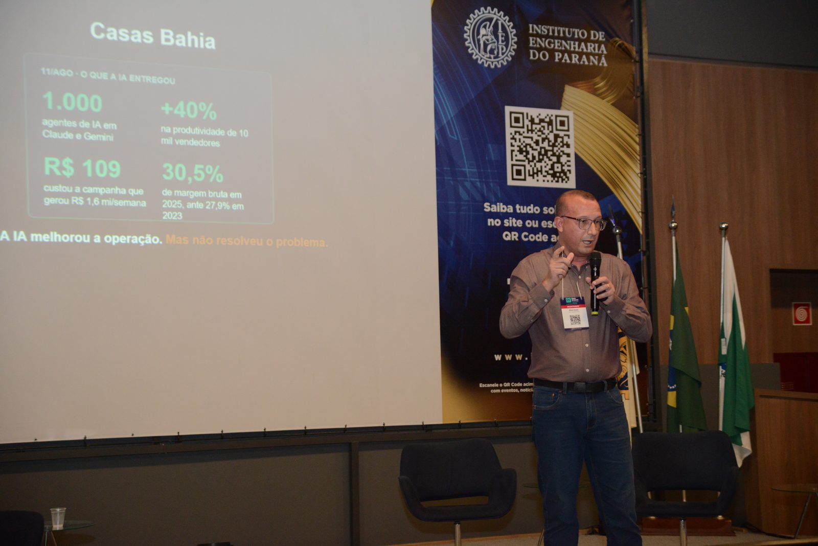 Alex Assis no palco do DSSBR 2026, diante do slide com resultados de IA da Casas Bahia
